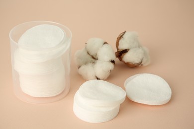 Photo of Container with cotton pads and flowers on beige background, closeup