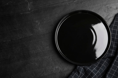 Photo of Empty plate and fabric on black table, flat lay. Space for text