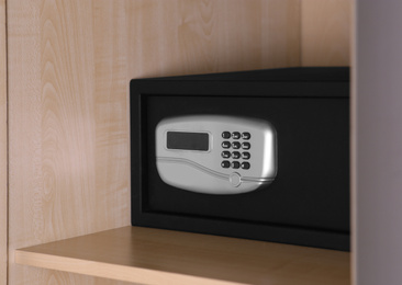 Photo of Black steel safe with electronic lock on wooden shelf