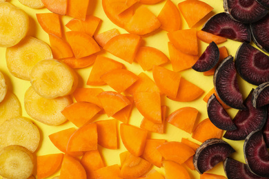 Photo of Pieces of raw color carrots on yellow background, flat lay