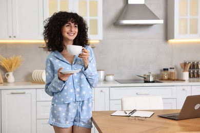 Photo of Beautiful young woman in stylish pyjama with cup of drink in kitchen