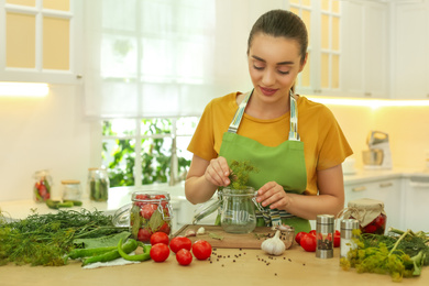 Photo of Woman putting dill into pickling jar at table in kitchen