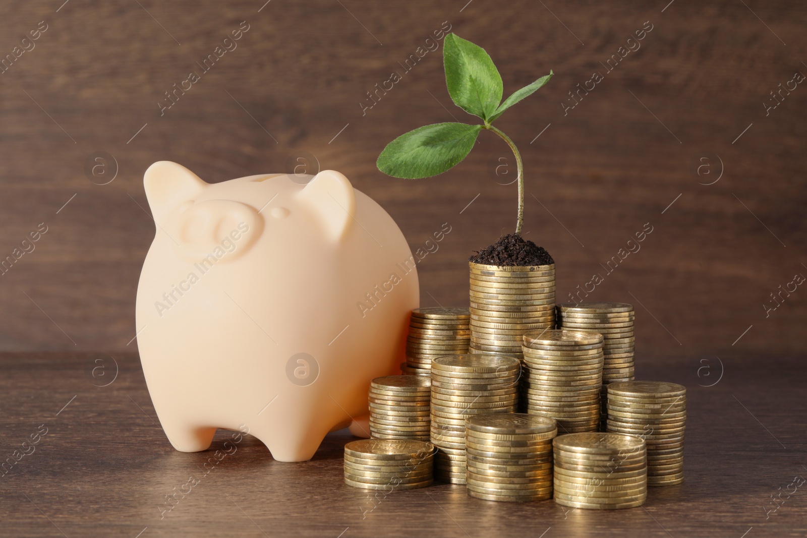 Photo of Stacks of coins with green sprout and piggy bank on wooden table. Investment concept