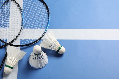 Photo of Feather badminton shuttlecocks and rackets on blue background, flat lay. Space for text