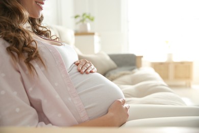 Pregnant woman touching her belly indoors, closeup