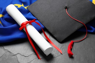 Photo of Graduation cap, diploma and flag of European Union on black table