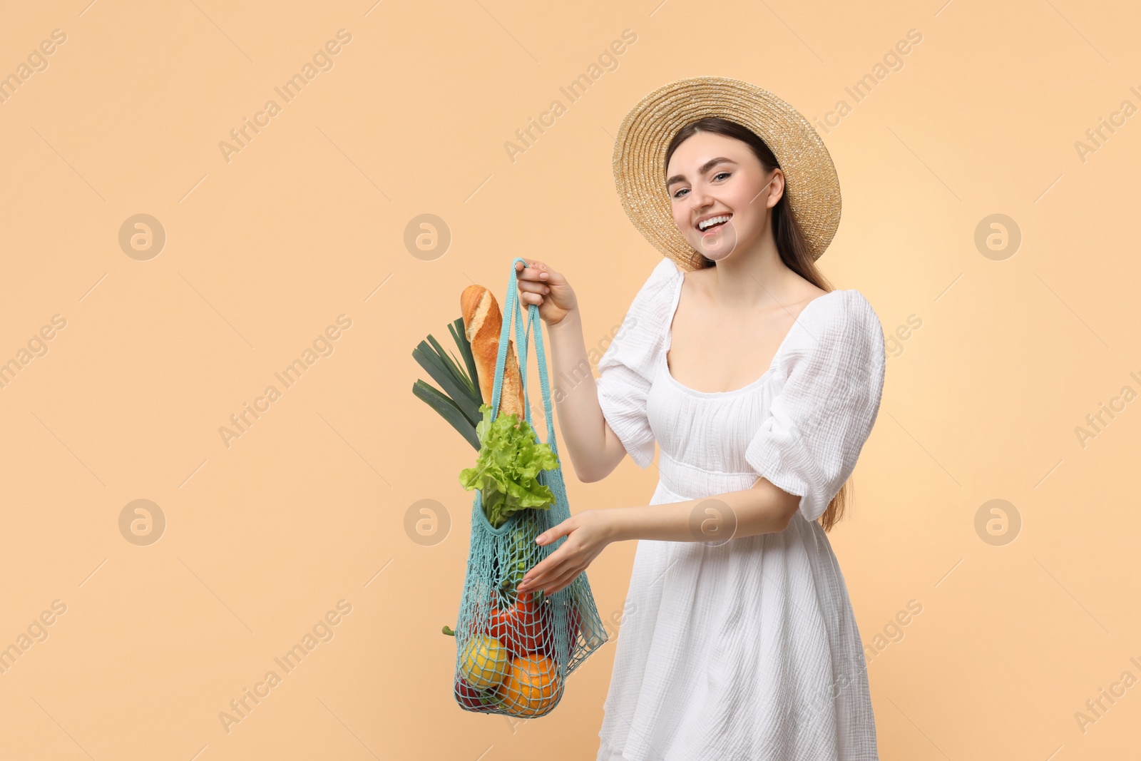 Photo of Woman with string bag of fresh vegetables and baguette on beige background, space for text