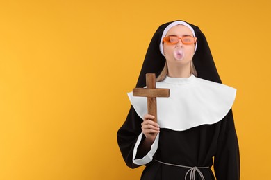 Photo of Woman in nun habit and sunglasses blowing bubble gum against orange background. Space for text