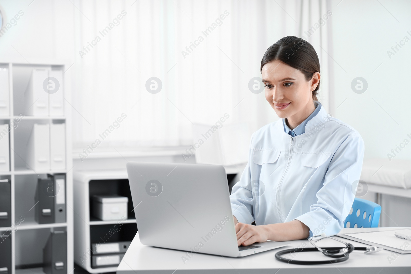 Photo of Young female doctor working with laptop at table in office