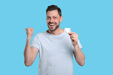 Photo of Emotional man holding condom on light blue background