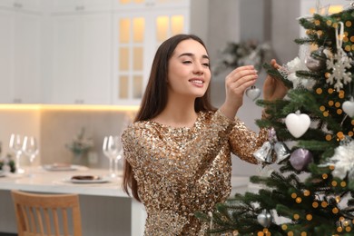 Photo of Smiling woman decorating Christmas tree with baubles in kitchen. Space for text