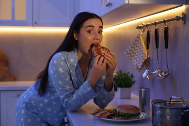 Photo of Young woman eating sandwich in kitchen at night. Bad habit