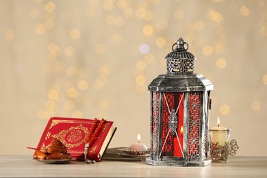 Photo of Arabic lantern, Quran, misbaha, candles and dates on wooden table against blurred lights