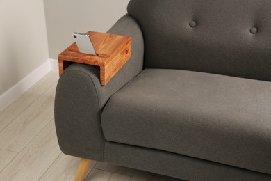 Photo of Smartphone on sofa with wooden armrest table in room. Interior element