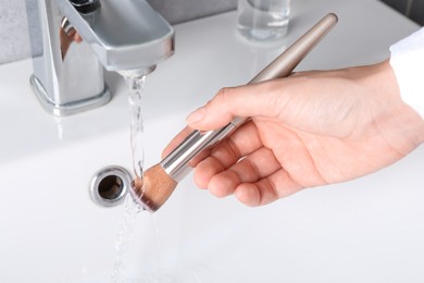 Photo of Woman washing makeup brush under stream of water in sink, closeup