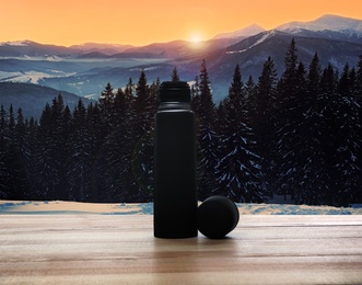 Image of Wooden desk with thermos and mountain landscape on background