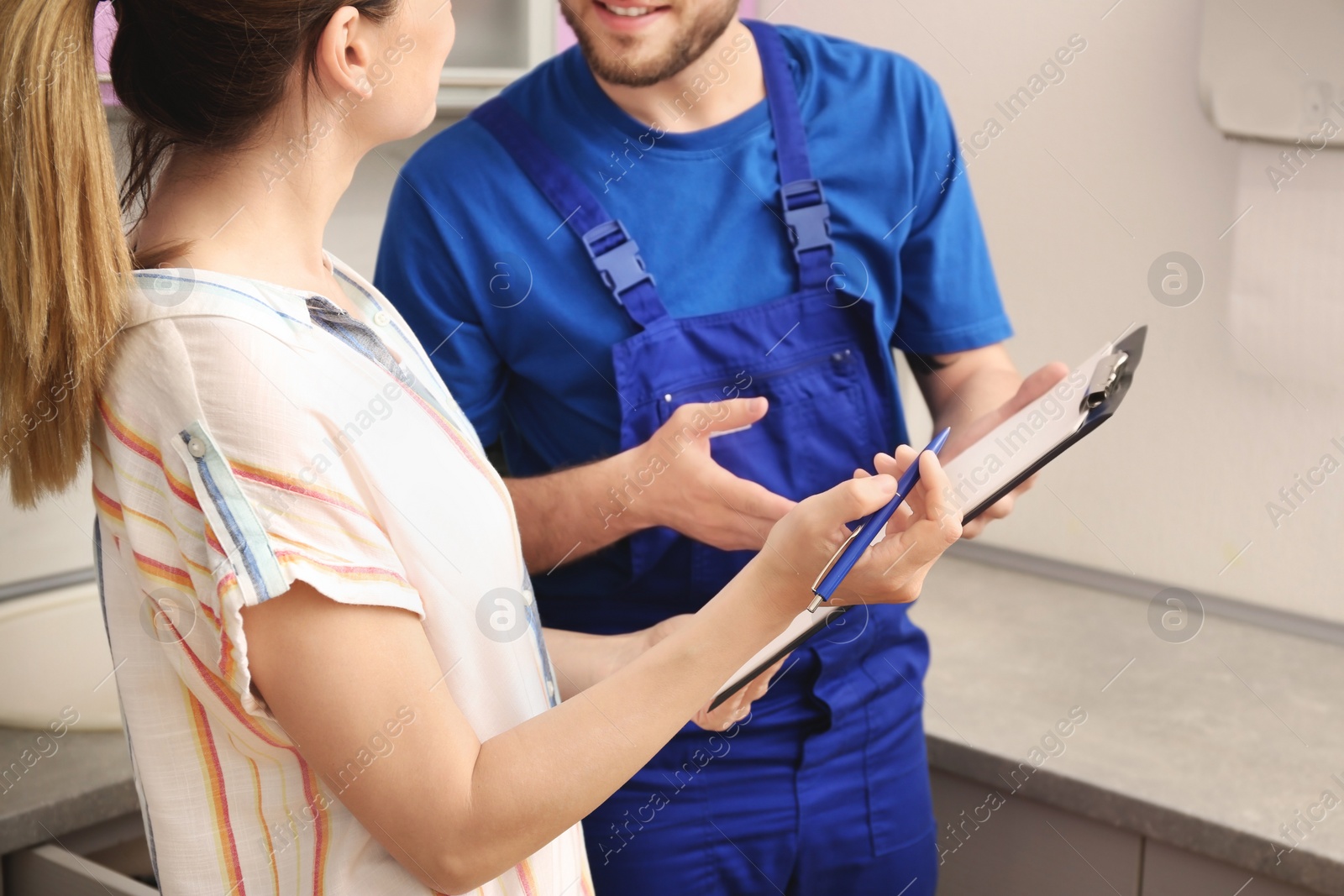 Photo of Professional plumber in uniform talking to client indoors