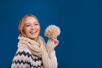 Photo of Young woman in warm sweater and scarf on blue background, space for text. Winter season