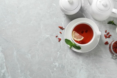 Photo of Cup of healthy goji tea with lemon on grey table, flat lay. Space for text
