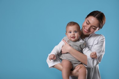 Photo of Young pediatrician with cute little baby on light blue background. Space for text