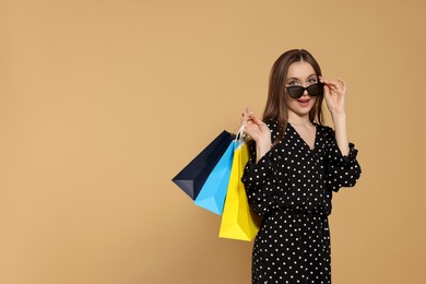 Photo of Stylish young woman in sunglasses with shopping bags on beige background, space for text