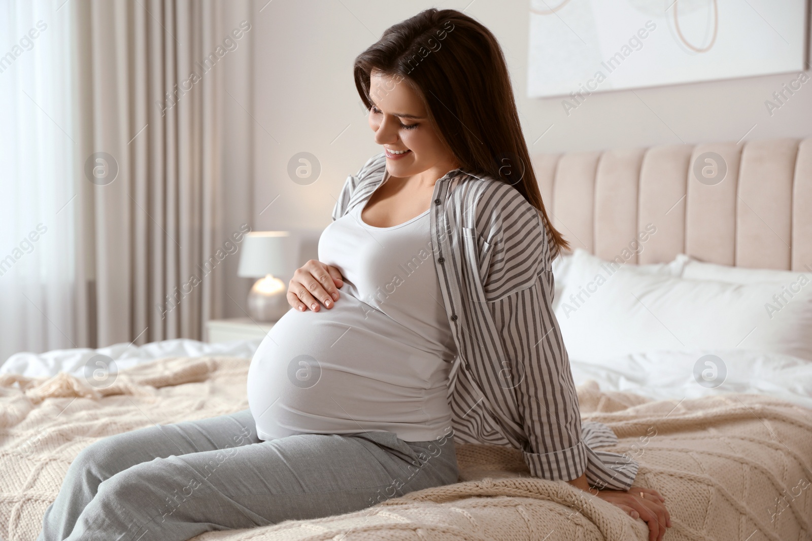 Photo of Young pregnant woman sitting on bed at home