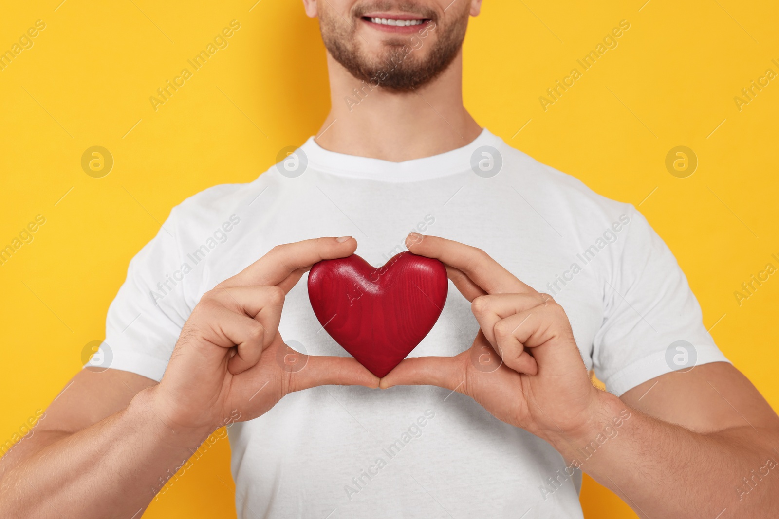 Photo of Happy volunteer holding red heart with hands on orange background, closeup