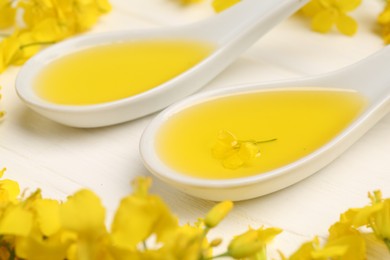 Photo of Rapeseed oil in gravy boats and beautiful yellow flowers on white wooden table, closeup