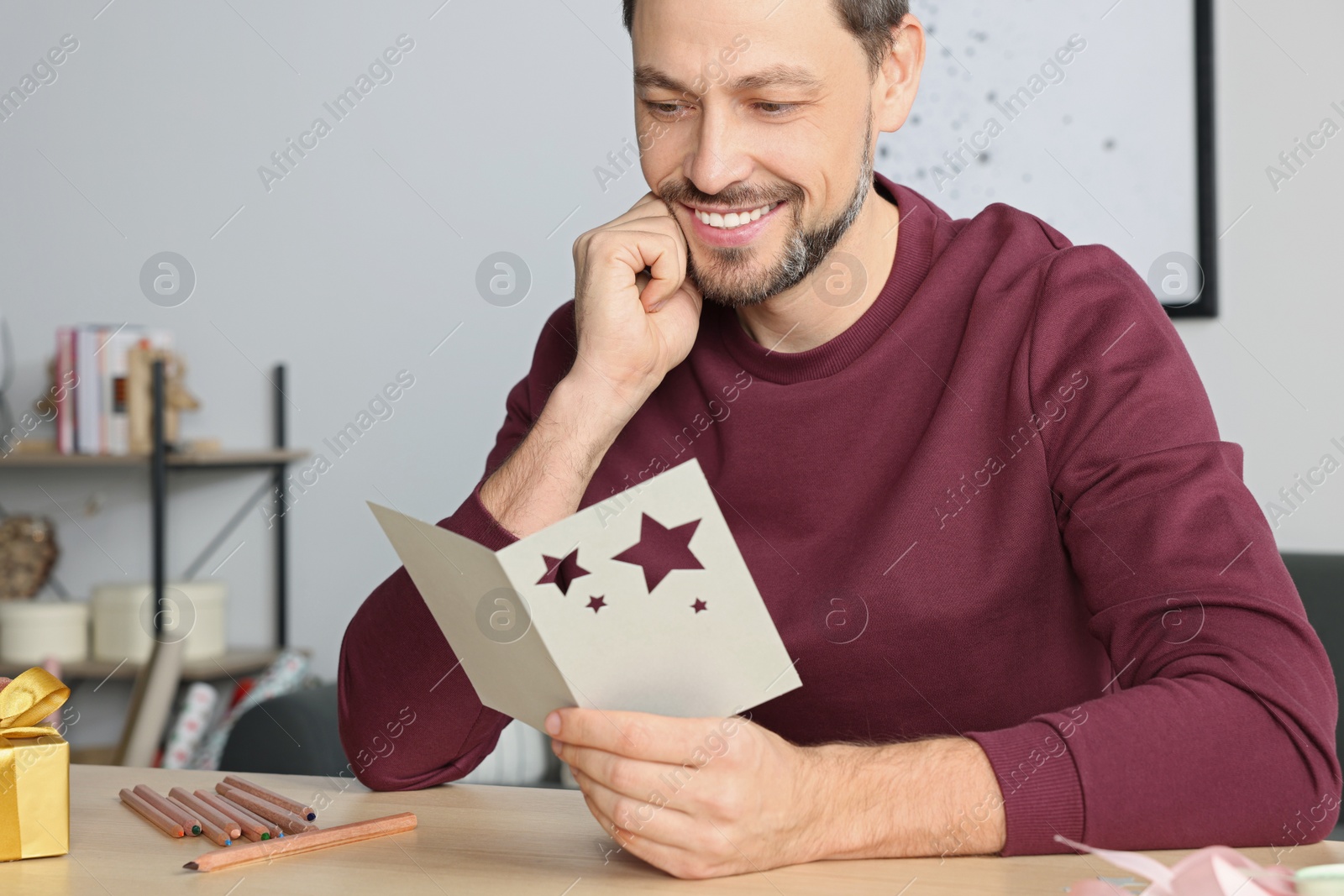 Photo of Happy man reading greeting card at wooden table in room