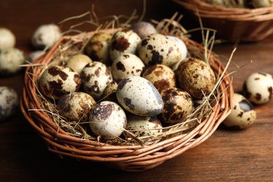 Photo of Wicker bowl with quail eggs and straw on wooden table, closeup