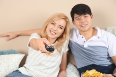 Young couple watching TV on sofa at home, focus on remote control