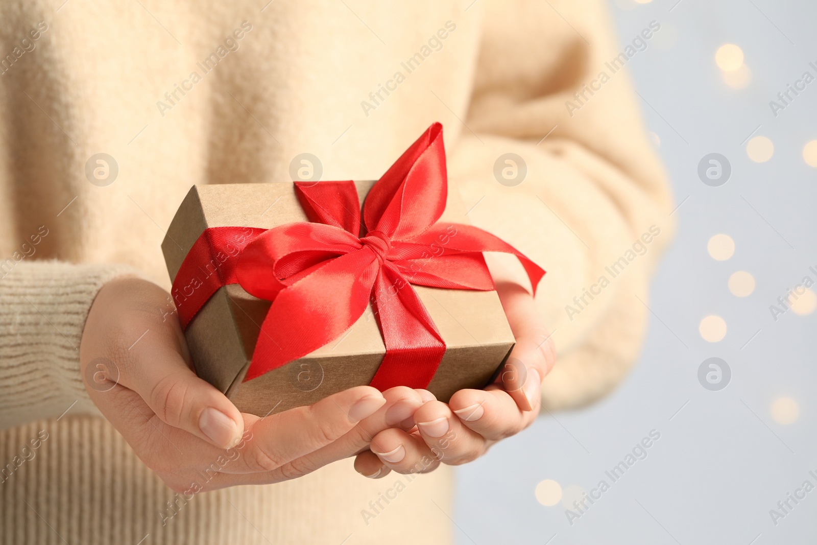 Photo of Woman holding gift box with red bow against blurred festive lights, closeup and space for text. Bokeh effect