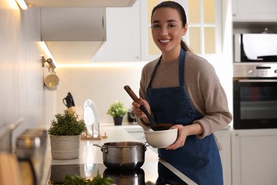 Smiling woman pouring tasty soup into bowl at countertop in kitchen