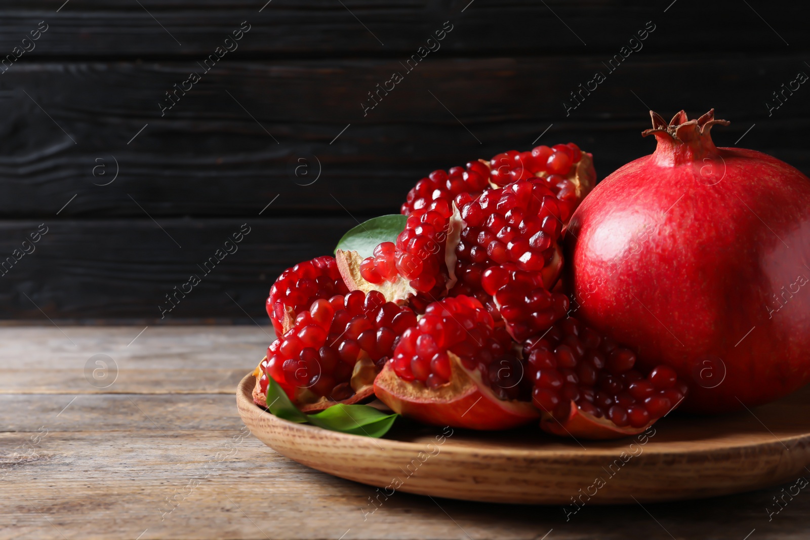 Photo of Plate with ripe pomegranates on wooden table against dark background, space for text