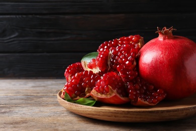 Photo of Plate with ripe pomegranates on wooden table against dark background, space for text