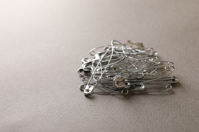 Pile of safety pins on light grey textured background, space for text