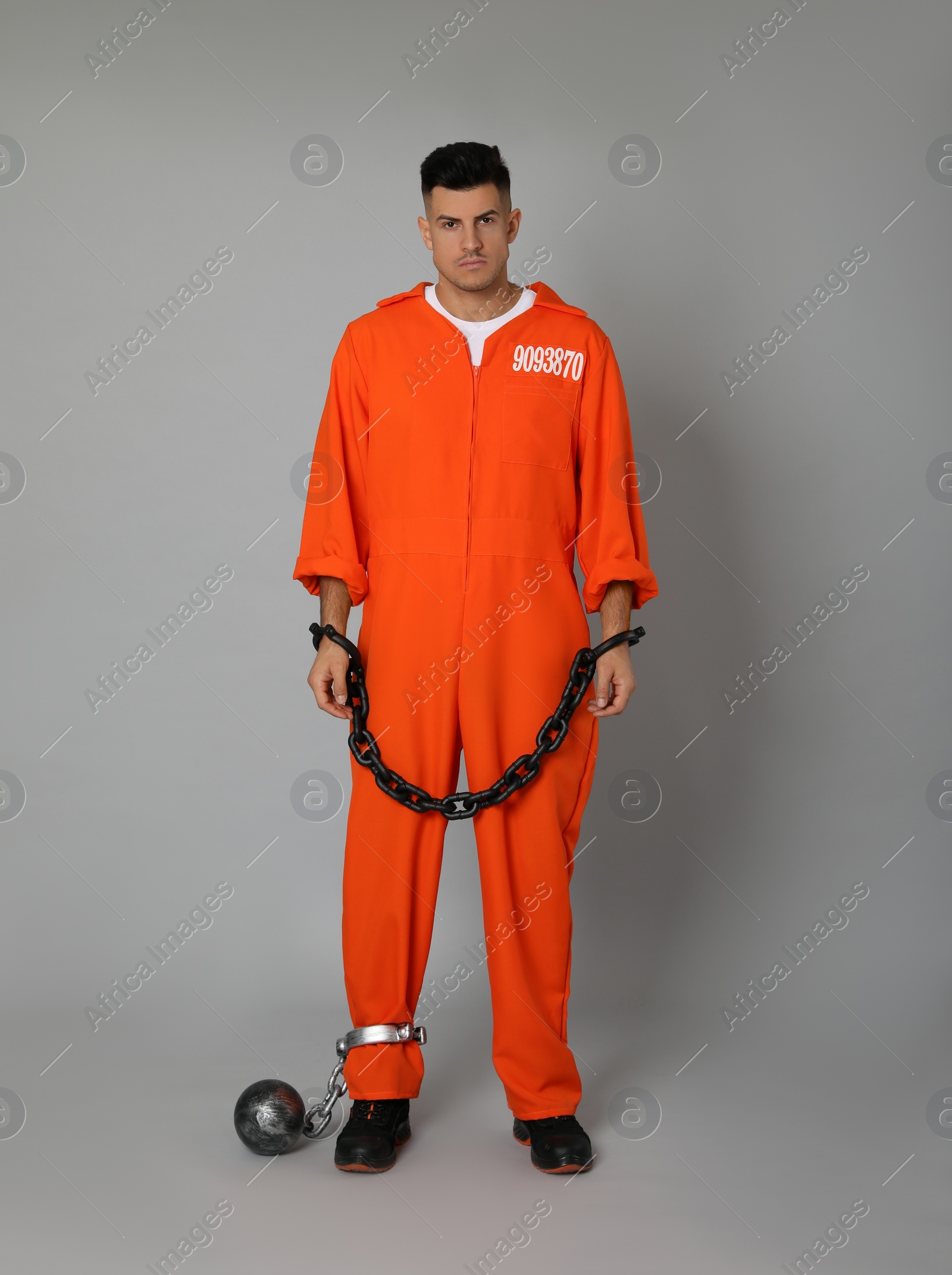 Photo of Prisoner in jumpsuit with chained hands and metal ball on grey background