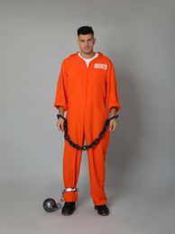 Photo of Prisoner in jumpsuit with chained hands and metal ball on grey background