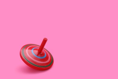 Photo of One bright spinning top on pink background, space for text. Toy whirligig