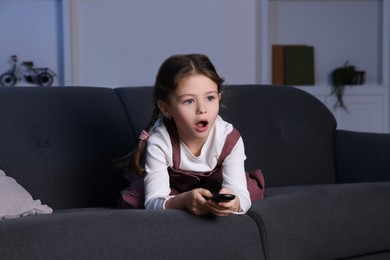Shocked girl watching TV on sofa at home