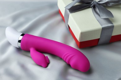 Photo of Gift box and pink vaginal vibrator on grey silk fabric. Sex toy