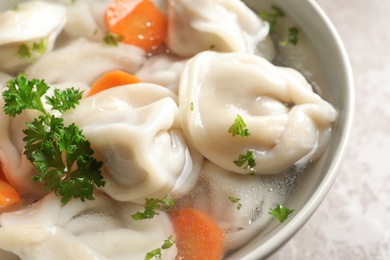 Photo of Bowl of tasty dumplings in broth on table, closeup