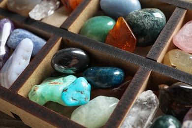 Box with different beautiful gemstones on table, closeup