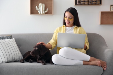 Photo of Young woman with eye patches working on laptop near her dog in living room. Home office concept