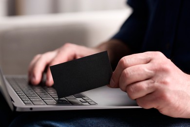 Photo of Man with laptop holding blank business card on blurred background, closeup