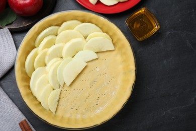 Photo of Flat lay composition with dish of fresh apple slices and raw dough on black table. Baking pie