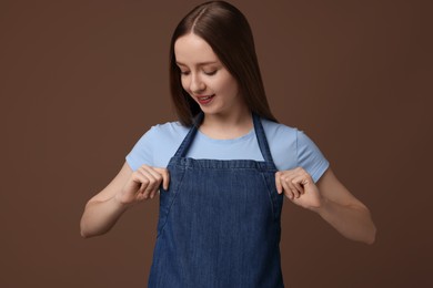 Photo of Beautiful young woman wearing kitchen apron on brown background. Mockup for design
