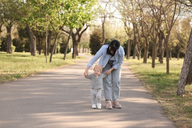 Photo of Mother supporting her baby while he learning to walk outdoors. Space for text