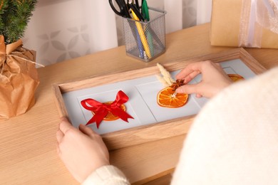 Photo of Woman making Christmas decor with dry orange slices at wooden table indoors, closeup