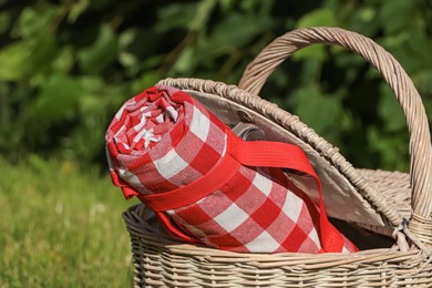 Rolled checkered tablecloth in picnic basket outdoors, closeup